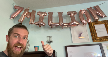 Zach pointing to the new balloons in his office that say 7 Million