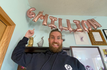 Zach pointing to the new balloons in his office that say 6 Million